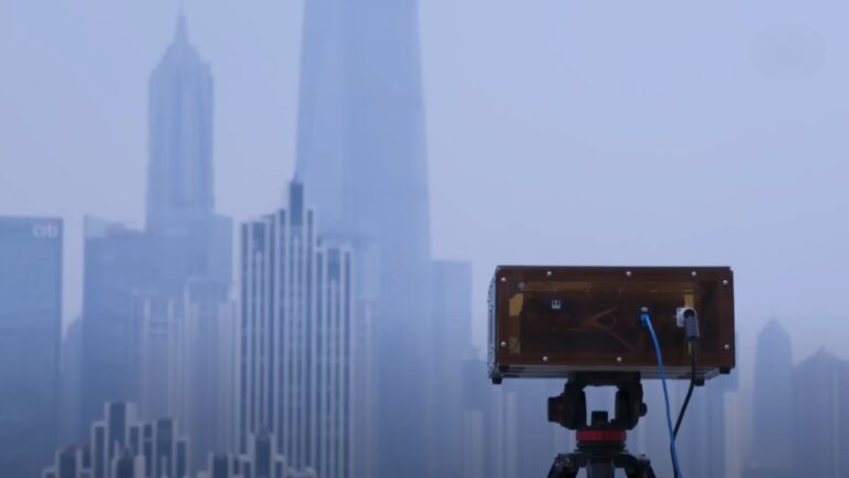 A Mantis Computer Mounted on A Tripod, Set Against a Backdrop of A Hazy City Skyline with Prominent Skyscrapers