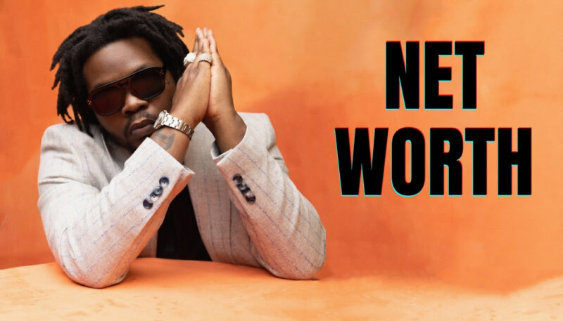 Olamide posing in a stylish suit against an orange background with 'Net Worth' text