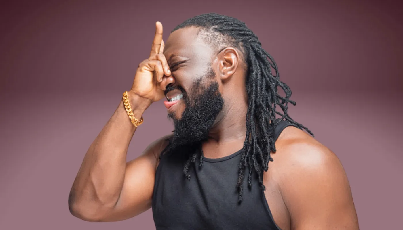 A joyful individual with dreadlocks wearing a tank top and a gold bracelet, striking a playful pose against a neutral background