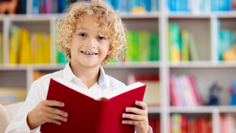 A smiling child holds an open book in a bright classroom, ready to learn about climate change