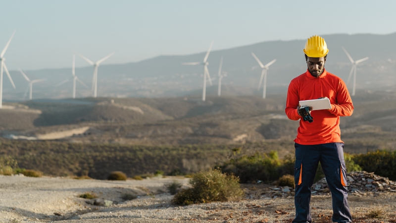 Man in hard hat views tablet at wind farm