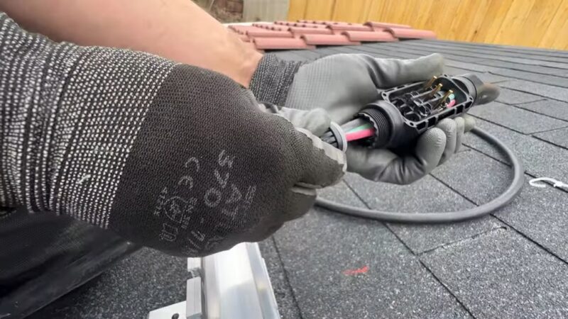 Gloved hands assembling and securing solar electrical wiring connectors on a rooftop