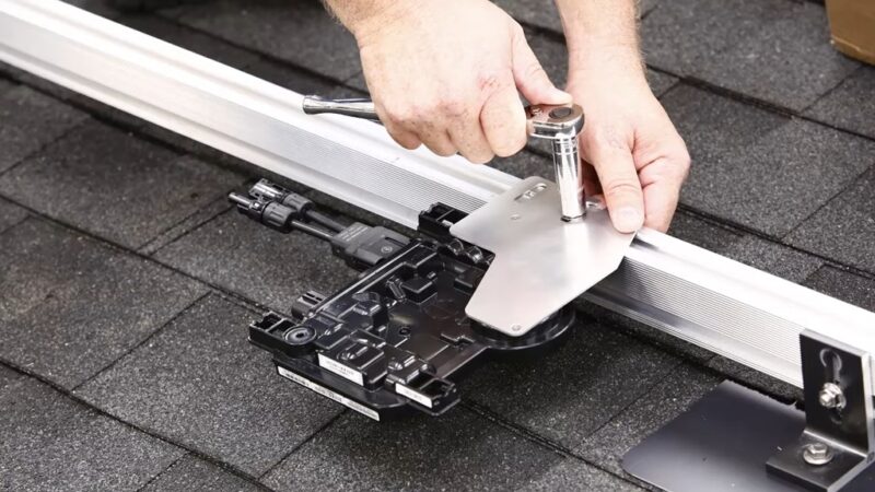 Solar installer using a ratchet tool to mount a microinverter on roof rails