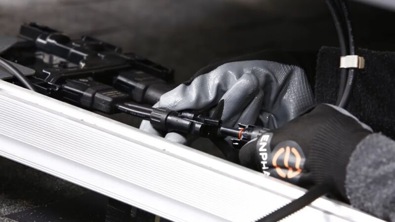 Close-up of Enphase-branded gloves connecting solar cables to a microinverter