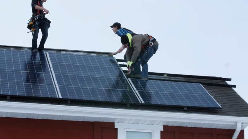 Team of technicians securing large solar panels on a rooftop in cold weather