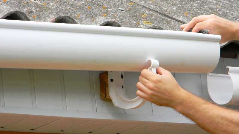 Person installing a white gutter system as part of smart design and placement for roof drainage and rainwater storage
