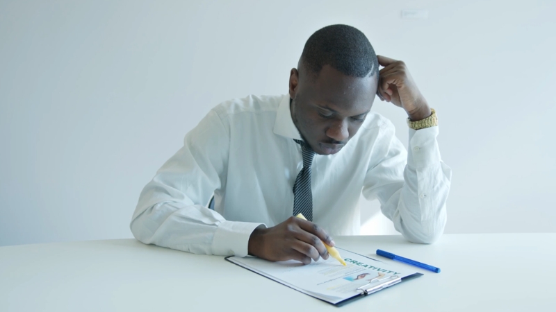 A man in business attire reviews documents at a desk in a bright office, focusing on planning a small business