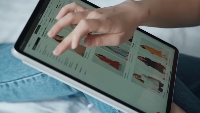 A person browses clothing products on a tablet screen while shopping online through a cross-border e-commerce store
