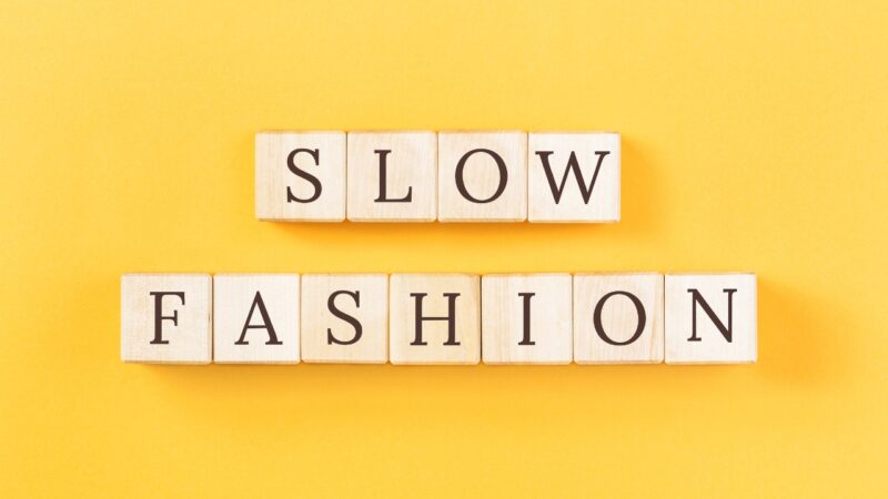 Wooden letter tiles spell slow fashion on a bright yellow background