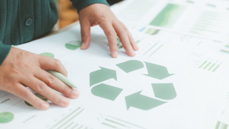 Hands review sustainability charts with a recycling symbol on the page