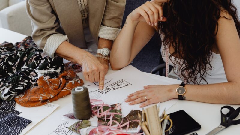 Two people review clothing sketches and fabric samples at a work table